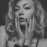 Beauty-Porträt von Mia mit Händen am Gesicht und sichtbarem Tattoo an der Schulter, Schwarz-Weiß