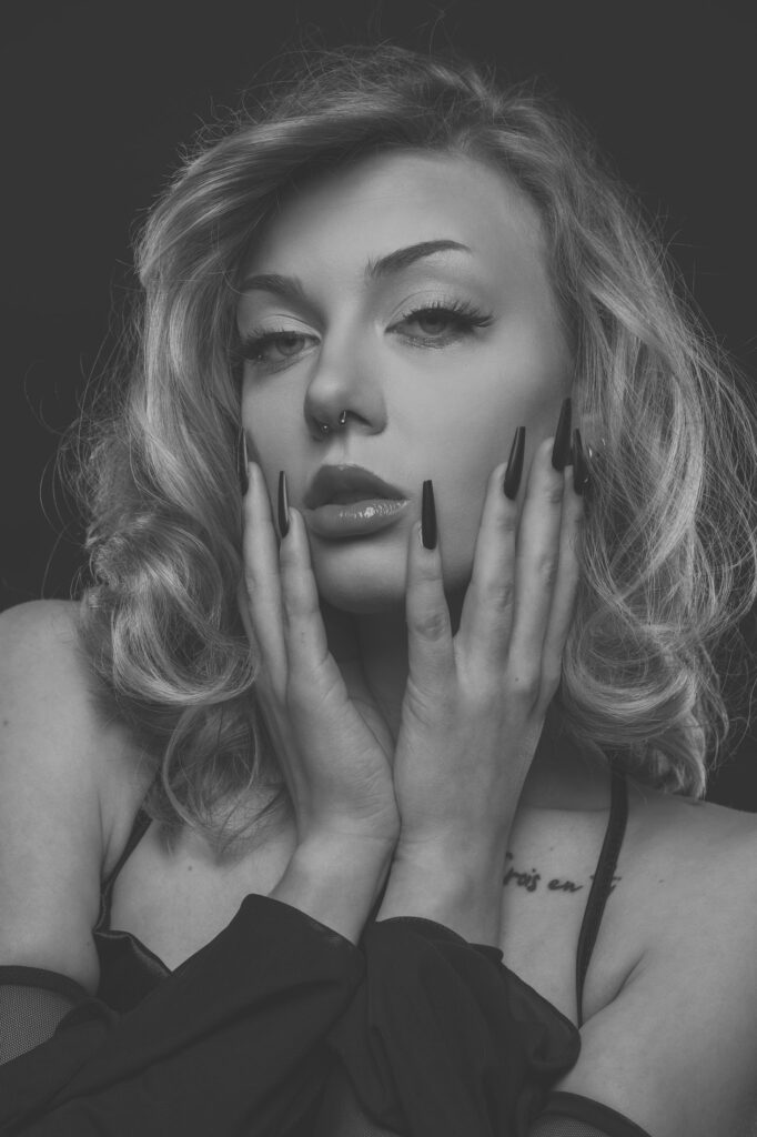 Beauty-Porträt von Mia mit Händen am Gesicht und sichtbarem Tattoo an der Schulter, Schwarz-Weiß