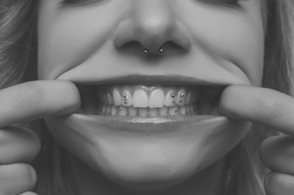 Nahaufnahme von Mias Lächeln mit Zahnschmuck und Septum-Piercing, Schwarz-Weiß