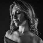 Schwarz-Weiß-Portrait von Alina im Studio: Nahaufnahme mit gesenktem Blick, offene Locken und feine Halskette