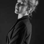 Schwarz-Weiß-Portrait von Alina im Studio: Seitenansicht im dunklen Blazer vor schwarzem Hintergrund