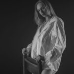 Schwarz-Weiß-Portrait von Annika im Studio: Ganzkörperaufnahme im weißen Oversize-Hemd an einer Stuhllehne