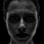Schwarz-Weiß-Portrait von Evelyn: frontales Low-Key-Portrait mit streng zurückgekämmtem Haar und Lichtakzenten auf dem Gesicht