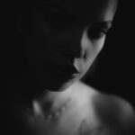 Schwarz-Weiß-Portrait von Lilly im Studio: Gesicht halb im Schatten, Perlenkette und Schulter-Tattoo