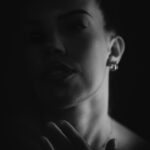 Schwarz-Weiß-Portrait von Lilly im Studio: Low-Key-Aufnahme mit Hand am Hals und Lichtakzent auf dem Gesicht