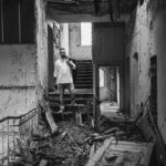 Schwarz-Weiß-Portrait von Paddy an einem Lost Place: Mann steht in einem verfallenen Innenraum mit alter Treppe