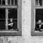 Schwarz-Weiß-Paarportrait von Sternchen und Paddy an einem Lost Place: beide schauen aus zwei Fenstern eines alten Hauses