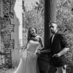 Schwarz-Weiß-Paarportrait von Sternchen und Paddy an einem Lost Place: Paar zwischen Steinsäulen, sie im weißen Kleid